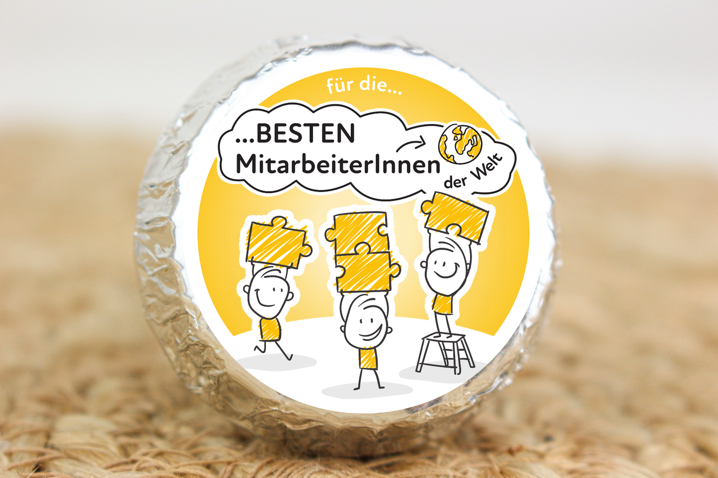 Silber verpackter Schokotaler mit Strichmännchen auf Siegerpodesten und Aufschrift „Für die besten MitarbeiterInnen der Welt“