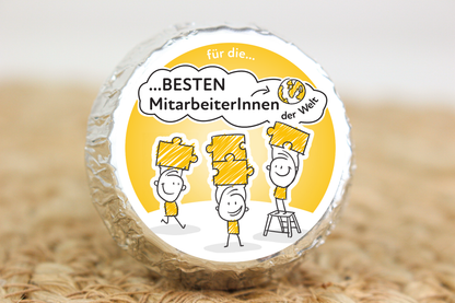 Silber verpackter Schokotaler mit Strichmännchen auf Siegerpodesten und Aufschrift „Für die besten MitarbeiterInnen der Welt“