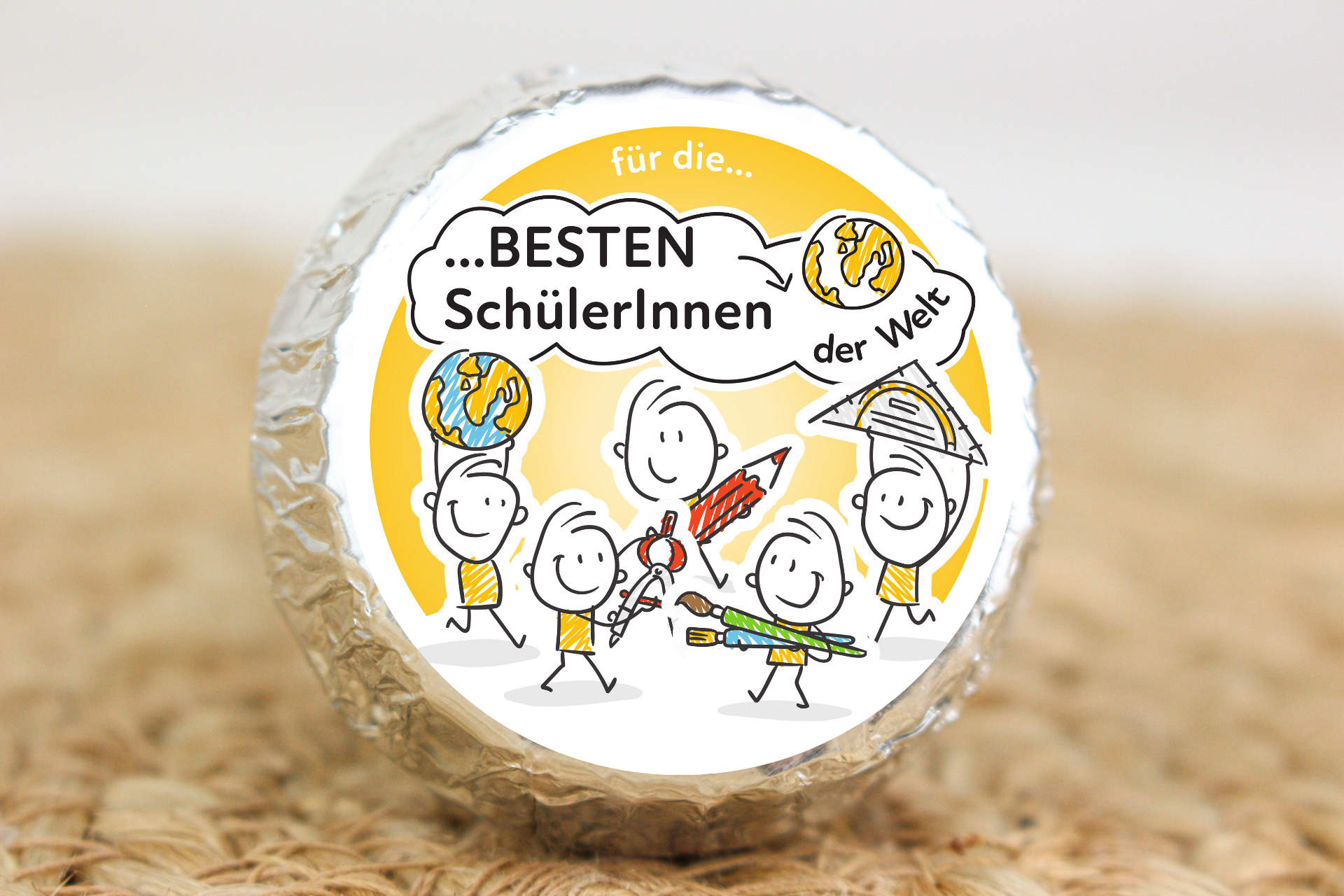 Silber verpackter Schokotaler mit Strichmännchen und Schulmotiven sowie Aufschrift „Für die besten SchülerInnen der Welt“