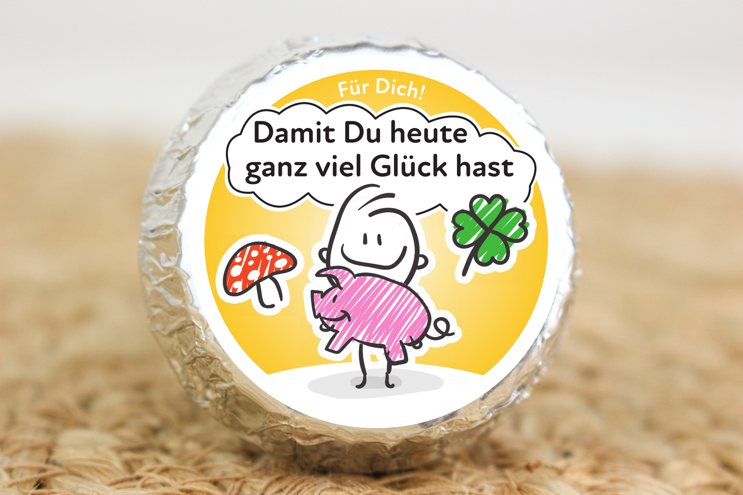 Silber verpackter Schokotaler mit Strichmännchen, Glücksschwein, Kleeblatt und Aufschrift „Damit du heute ganz viel Glück hast“