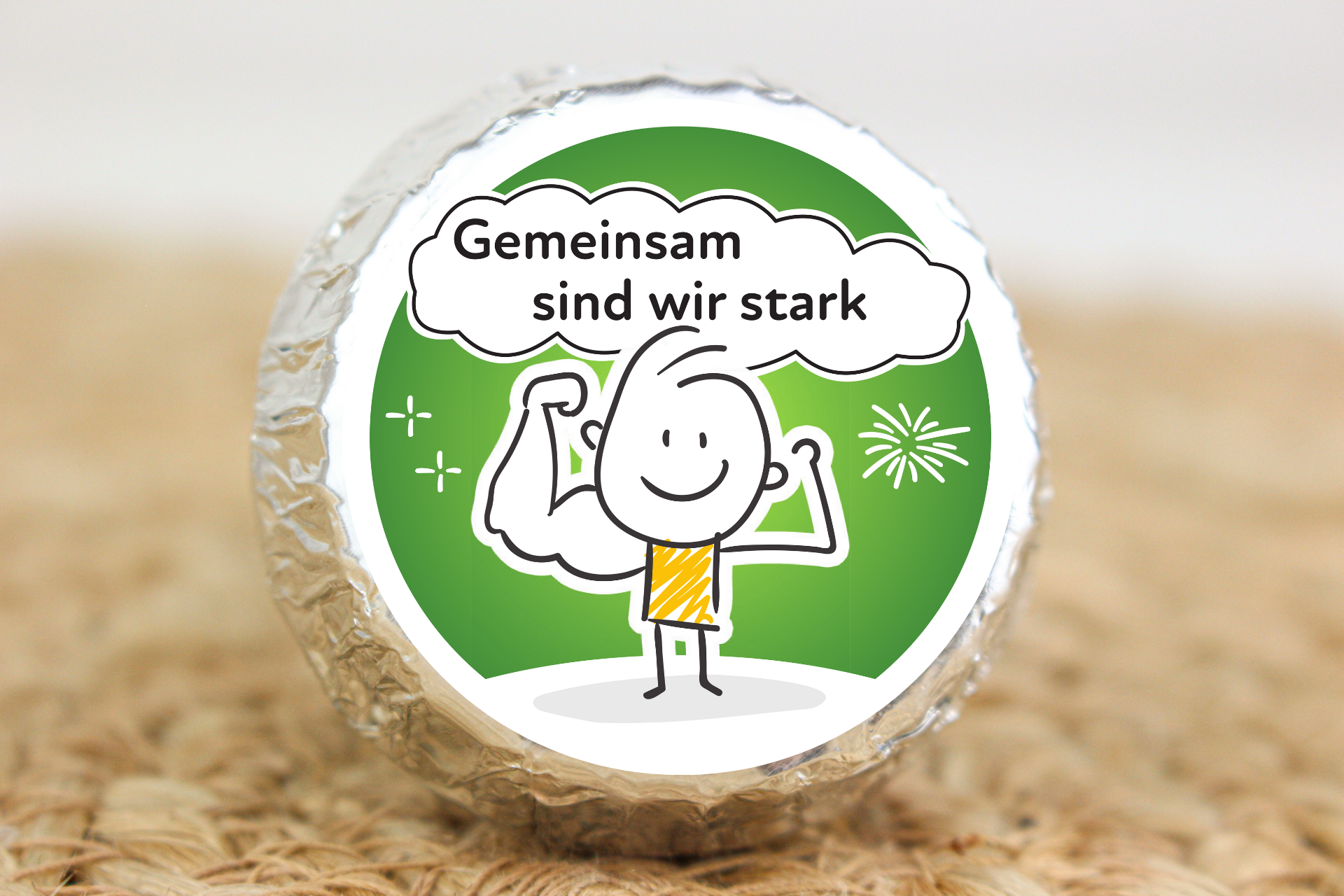 Silber verpackter Schokotaler mit starkem Strichmännchen und Aufschrift „Gemeinsam sind wir stark“